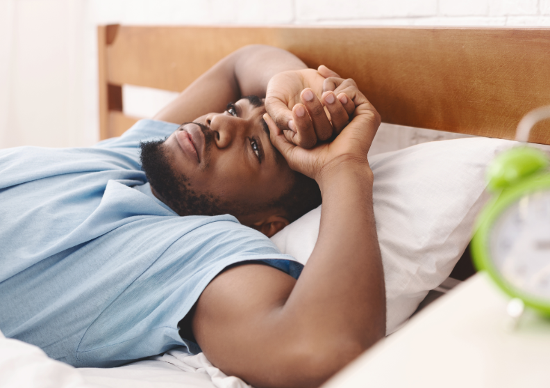 Man lying in bed looking tired with alarm clock in foreground