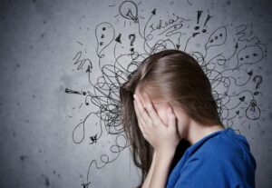 Woman with hands over face in front of wall with scribbles drawn around her head